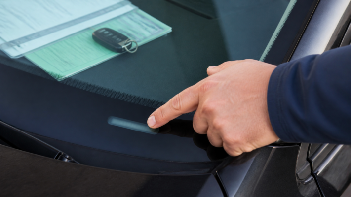 Finger zeigt auf unleserliche Fahrgestellnummer an der Windschutzscheibe